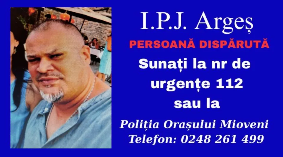 Un bărbat cu păr scurt și barbă căpătată poartă un tricou gri și un lanț argintiu pe un fundal albastru cu text alb și roșu.