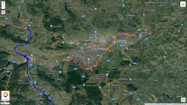 O hartă satelit de la înălțime arată o zonă urbană înconjurată de terenuri verzi, cu linii colorate marcate pe trasee rutiere.