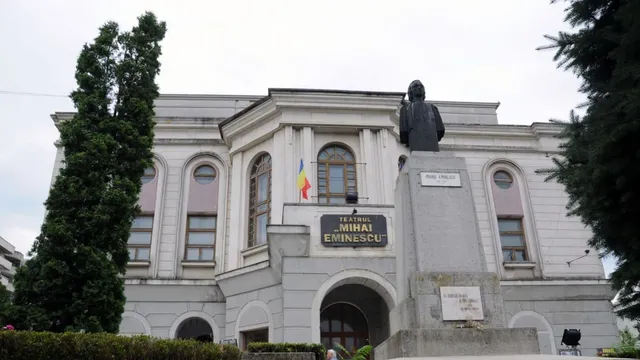 O clădire cu ferestre înalte și un bust sculptat pe un soclu înalt în prim-plan.