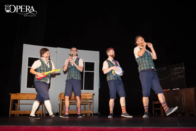 Patru bărbați în costume de scenă, veste și pantaloni scurți, execută o reprezentație pe o scenă de teatru în fața unui fundal alb.