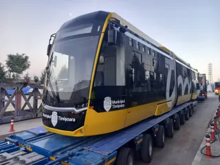 Un tramvai galben și negru cu inscripția Municipiul Timișoara este transportat pe o platformă de marfă cu mai multe roți.