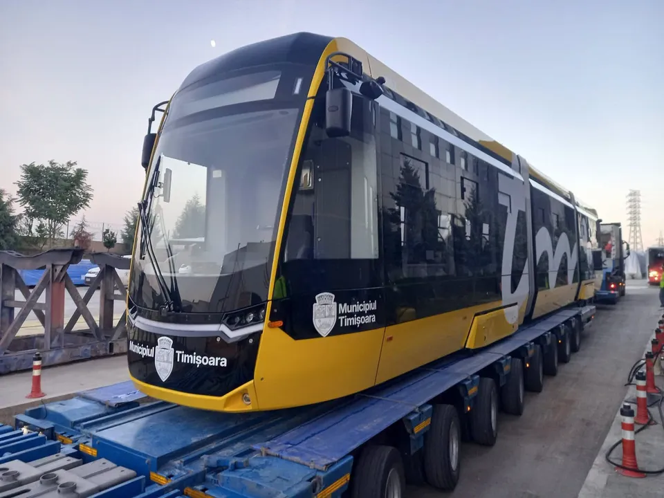 Un tramvai galben și negru cu inscripția Municipiul Timișoara este transportat pe o platformă de marfă cu mai multe roți.