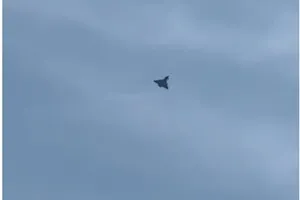 O siluetă întunecată de avion zboară pe un cer acoperit de nori gri.