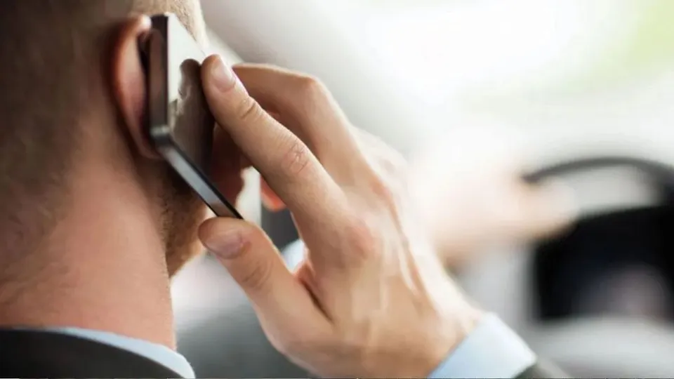 Un bărbat ține un telefon mobil lângă ureche, fiind surprins din profil cu mâna ridicată spre dispozitiv.