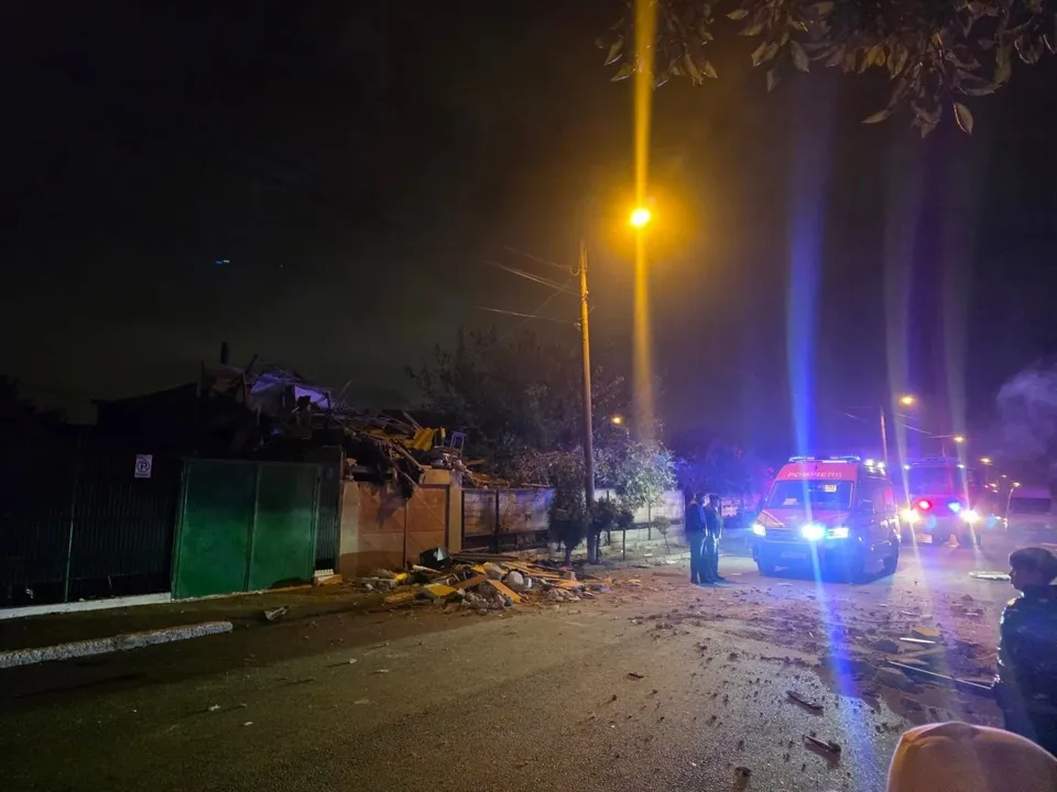 O mașină de serviciu cu lumini albastre este parcată pe un drum de noapte lângă o clădire cu resturi împrăștiate pe sol.