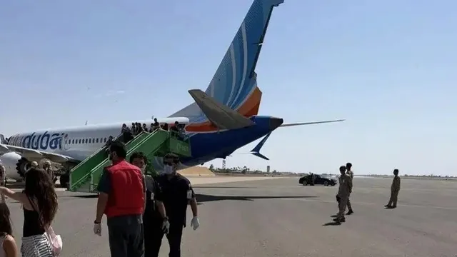O grupă de persoane coboară pe o scară verde de lângă coada unui avion alb cu dungi albastre și portocalii pe o pistă de aterizare.