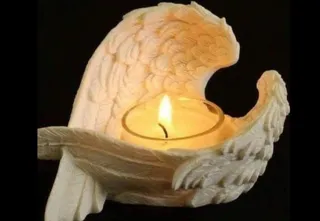 O lumânare aprinsă este așezată într-un suport sculptat sub forma unor aripi de îngeri pe un fundal negru.