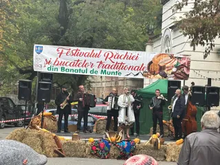 Un grup de muzicieni cântă pe o scenă decorată cu fân, având un banner cu text și imagini de mâncare deasupra lor.