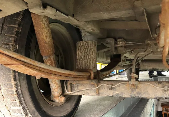 Partea inferioară a unui vehicul prezintă o arc de suspensie cu un bloc de lemn inserat între lamele acestuia.