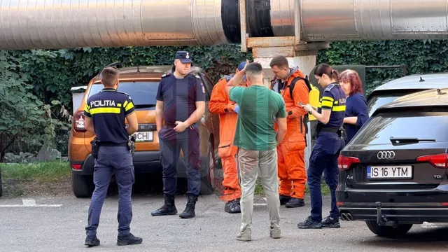 Mai mulți oameni în uniforme de poliție și echipamente de protecție portocalii stau pe o stradă lângă două mașini parcate.