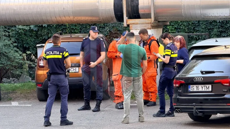 Mai mulți oameni în uniforme de poliție și echipamente de protecție portocalii stau pe o stradă lângă două mașini parcate.