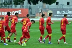 Cei mai mulți jucători de fotbal poartă echipamente roșii și galbene pe un teren de fotbal verde.
