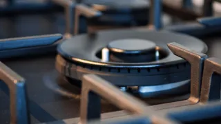 A close-up photograph of a black gas stove burner with metal grates, showing details of the cooking appliance.