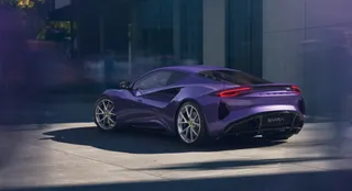 Un automobil sportiv de culoare mov este parcat pe o suprafață pavată în fața unei clădiri moderne sub lumina soarelui.