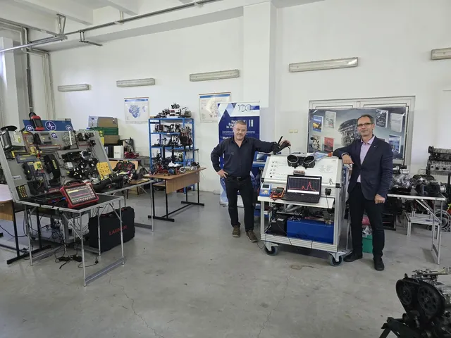 Doi bărbați stau într-un laborator lângă un echipament tehnic pe cărucior și mese cu diverse dispozitive electronice și componente mecanice.