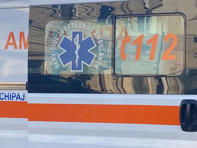 Un detaliu de pe un vehicul de serviciu prezintă un simbol medical albastru și numărul 112 scris cu caractere portocalii pe un fundal metalic.