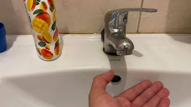 O mână este întinsă spre un lavoar alb lângă un robinet metalic și un recipient decorat cu fructe.