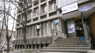 O clădire gri cu ferestre rectangulare, o scară de beton în prim-plan și un arbore fără frunze în partea stângă.