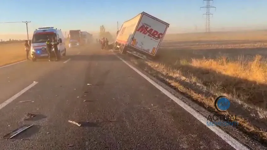 Un camion alb cu inscripții roșii este înclinat pe marginea unei drumuri asfaltate lângă o ambulanță și un autotren în lumină naturală de seară.