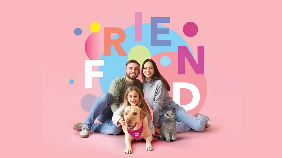 O familie formată din doi adulți și o copilă stă pe un fundal roz alături de un câine și o pisică.
