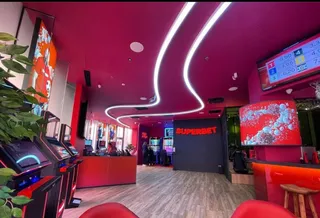 Interiorul unei încăperi cu tavan roșu, lumină neon curbată, aparate de jocuri de noroc și un ghișeu de recepție roșu.