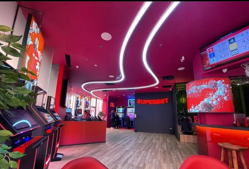 Interiorul unei încăperi cu tavan roșu, lumină neon curbată, aparate de jocuri de noroc și un ghișeu de recepție roșu.