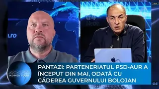 Un bărbat cu barbă și un bărbat cu părul scurt stau în fața unor ecrane albastre într-un studio de televiziune.