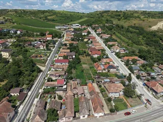 O vedere aeriană prezintă o zonă rezidențială cu case cu acoperișuri înclinate, drumuri și dealuri verzi sub un cer cu nori.