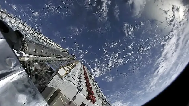 O parte dintr-o structură metalică cu componente circulare albe este poziționată în prim-plan, având curba planetei și nori în fundal.