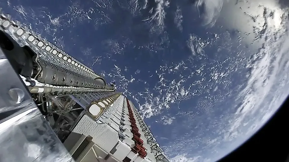 O parte dintr-o structură metalică cu componente circulare albe este poziționată în prim-plan, având curba planetei și nori în fundal.
