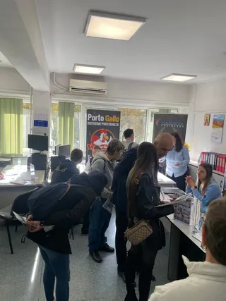Oamenii stau în picioare într-o încăpere cu mese, consultând documente lângă standuri de prezentare cu afișe și monitoare de calculator.