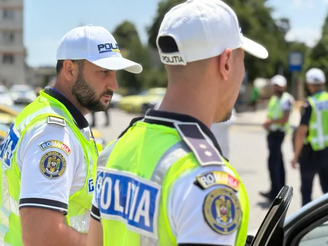 Doi polițiști în uniformă de un verde fosforescent și șapcă albă stau lângă o mașină pe un drum public.