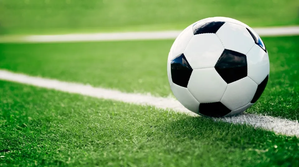 Un fotbal alb cu pete negre este plasat pe iarba verde a unui teren de fotbal lângă o linie albă.