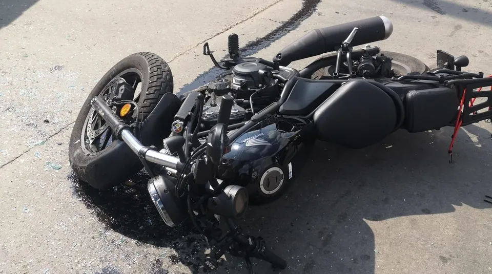 O motocicletă neagră este culcată pe asfaltul gri lângă o urmă de lichid întinsă pe sol.