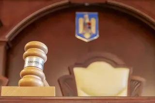 Un ciocan de lemn cu inscripția CONSTITUTION se află pe o masă în fața unui scaun de piele într-o încăpere din lemn.