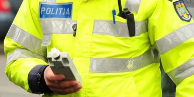 Un polițist în uniformă galbenă fluorescentă cu inscripția 'POLITIA' ține un etilotest electronic gri în mână.