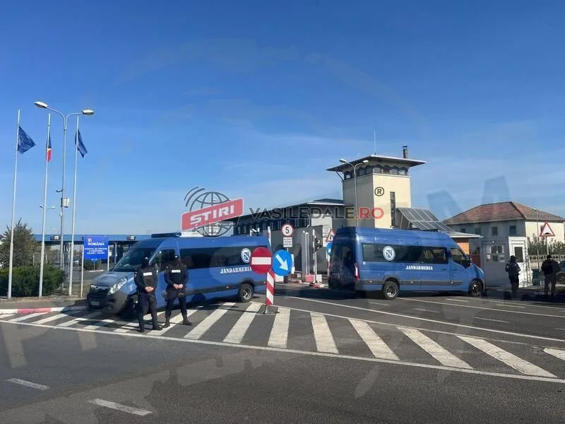 Două microbuze albastre sunt parcate pe un drum asfaltat lângă un punct de frontieră sub un cer senin.