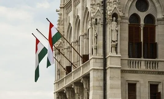 Trei steaguri tricolore verzi, albe și roșii sunt arborate pe o fațadă de clădire cu elemente arhitecturale clasice și sculpturi.