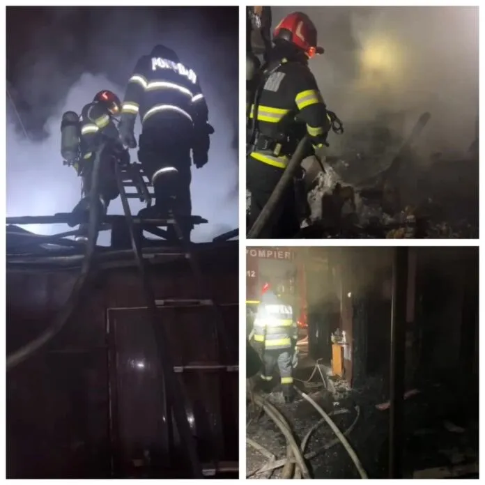 Pompieri în echipament de protecție și cu echipamente de respirație lucrează pe un acoperiș și printre resturi de deșeuri în condiții de fum.