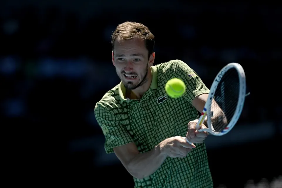 Un bărbat cu tricou verde în timp ce lovește o minge de tenis cu o racletă pe un teren de tenis.