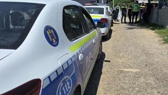Două mașini de poliție parcate pe un drum de pământ, cu mai mulți ofițeri în fundal.