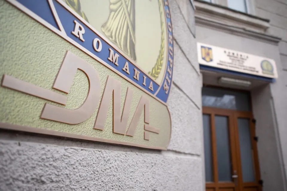 Un semn cu inscripția DNA și ROMANIA este montat pe o fațadă de clădire lângă o intrare cu uși de lemn.