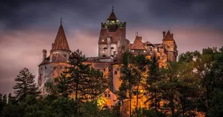 O cetate medievală cu turnuri înalte și acoperișuri conice este iluminată de lumină caldă sub un cer închis la culoare.