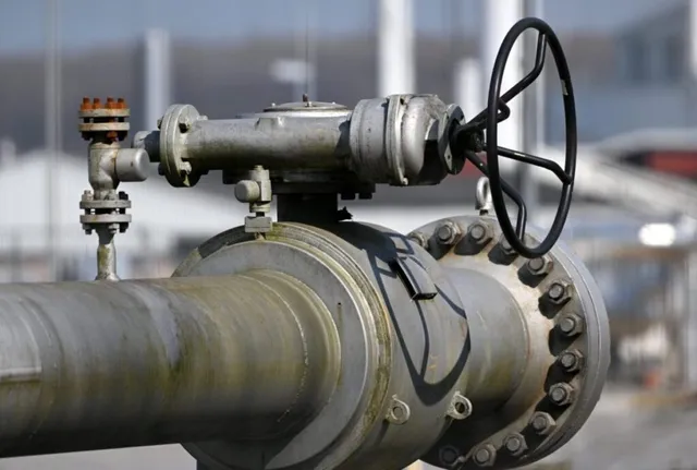 O supapă metalică cu o roată de control neagră este montată pe o conductă industrială gri sub un cer luminos.