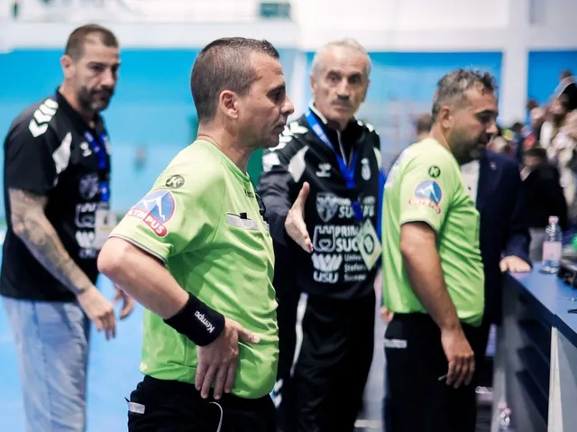 Un bărbat într-un tricou verde deschis stă cu mâinile pe șolduri într-o sală de sport lângă alți bărbați.