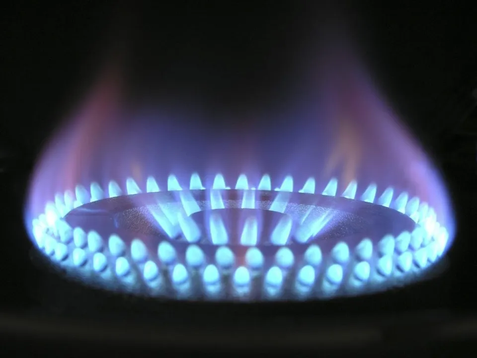 O flacără albastră arde pe un arzător de gaz de culoare închisă pe un fundal negru.