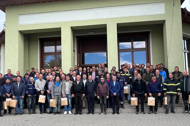 Un grup mare de bărbați stă în rând în fața unei clădiri verzi, mulți dintre ei ținând pungi de carton maro.