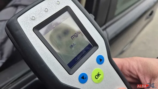 O mână ține un dispozitiv electronic cu un ecran care afișează text și unități de măsură.
