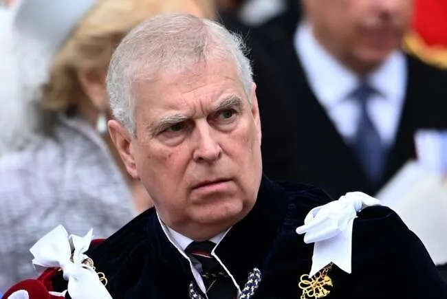 Un bărbat cu părul scurt și cărunt poartă o vestă neagră de catifea peste o cămașă albă cu cravată în culori închise.
