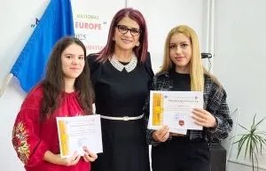 Trei femei stau în picioare, două dintre ele țin diplome albe cu detalii galbene și roșii.
